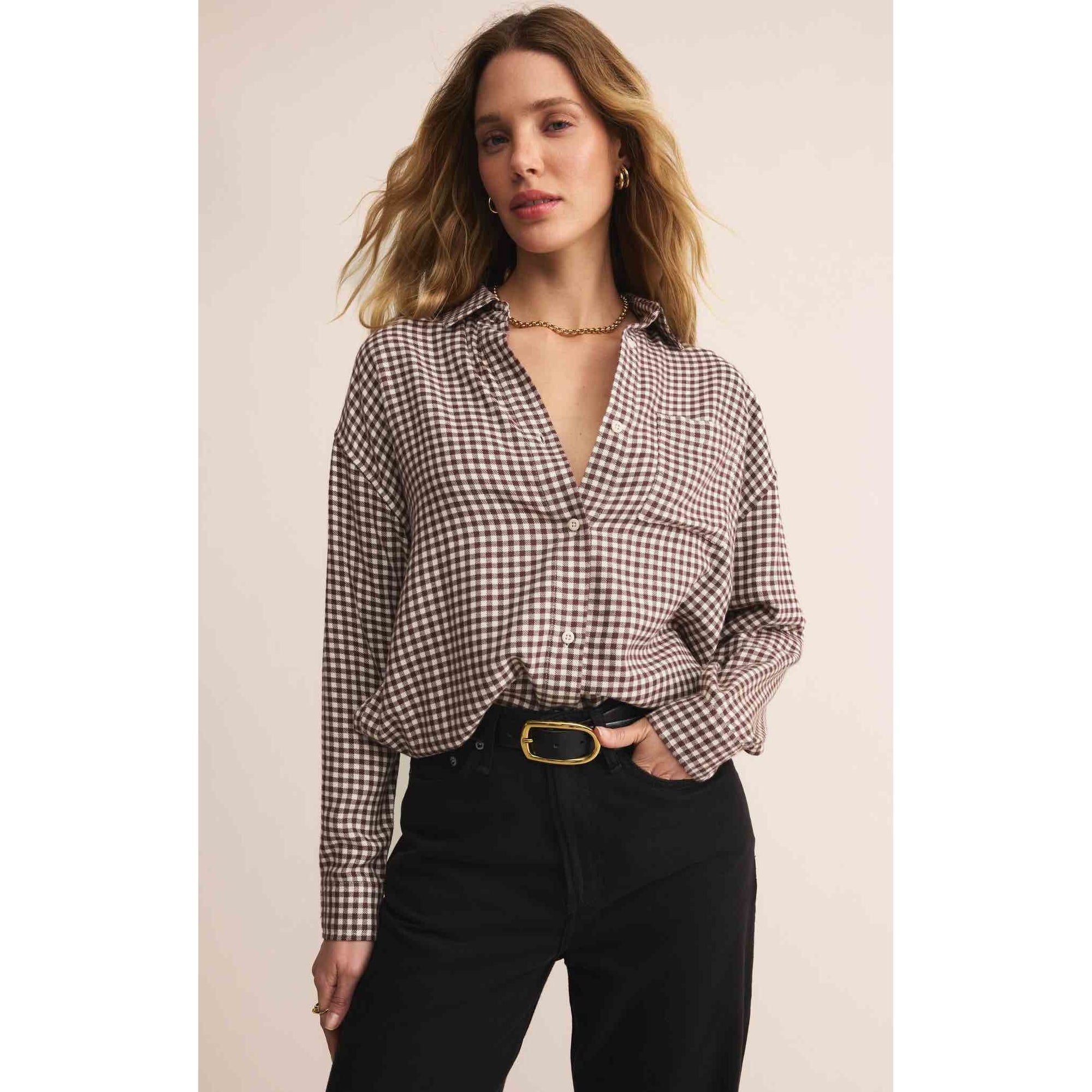 Woman wearing Z Supply River Plaid Button Up Top in brown-and-cream gingham with black pants and a gold belt.
