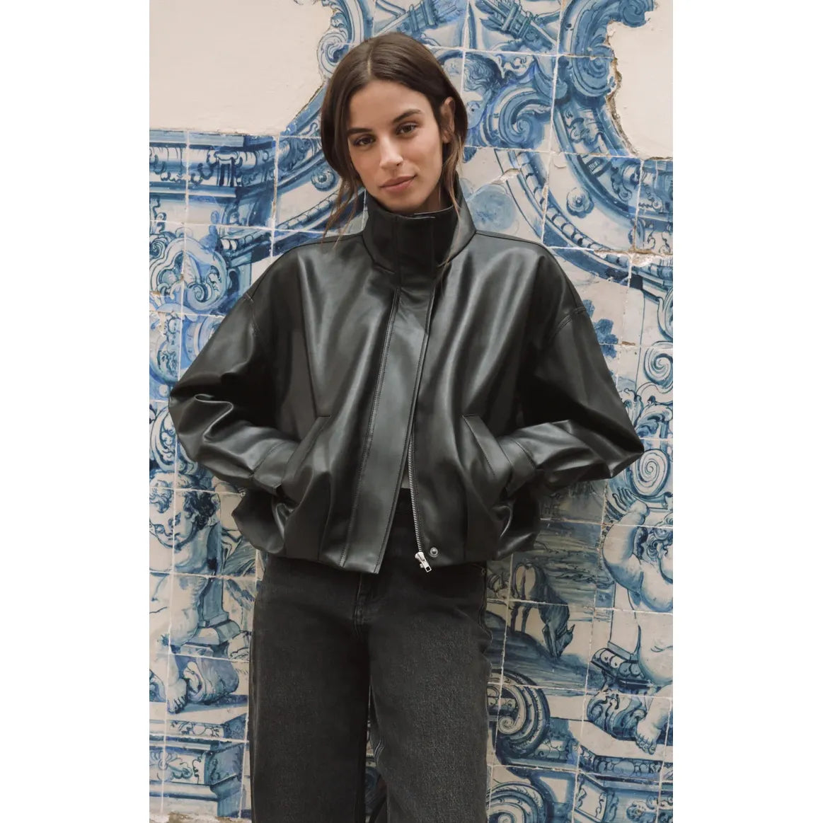 Black Z Supply Corin faux leather bubble jacket with a funnel neck and sculpted shape against a blue tiled wall.