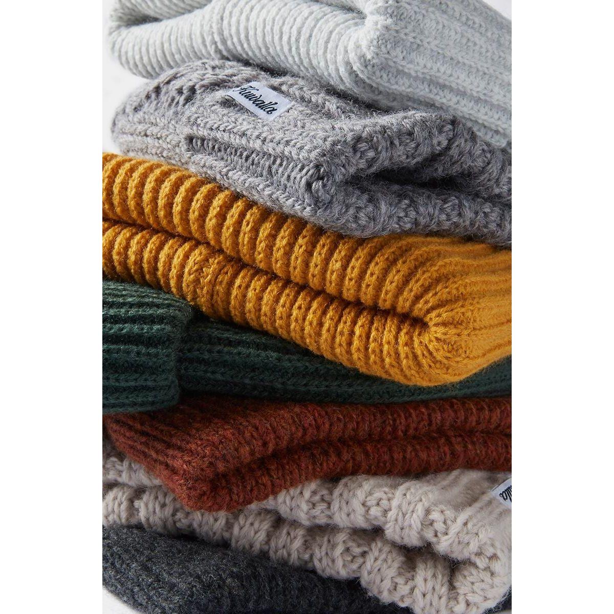 Kuwalla Essential Beanie: stacked acrylic knit hats in warm colors with brand tag.